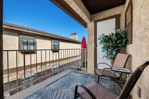 A balcony with a view of a building, a potted plant, and a table with chairs. - AT&T Stadium Area Arlington TX 1 Bed 1 Bath (Arlington)
