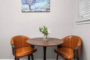 A dining area with two leather chairs, a round wooden table, and a vase with flowers. - AT&T Stadium Area Arlington TX 1 Bed 1 Bath (Arlington)