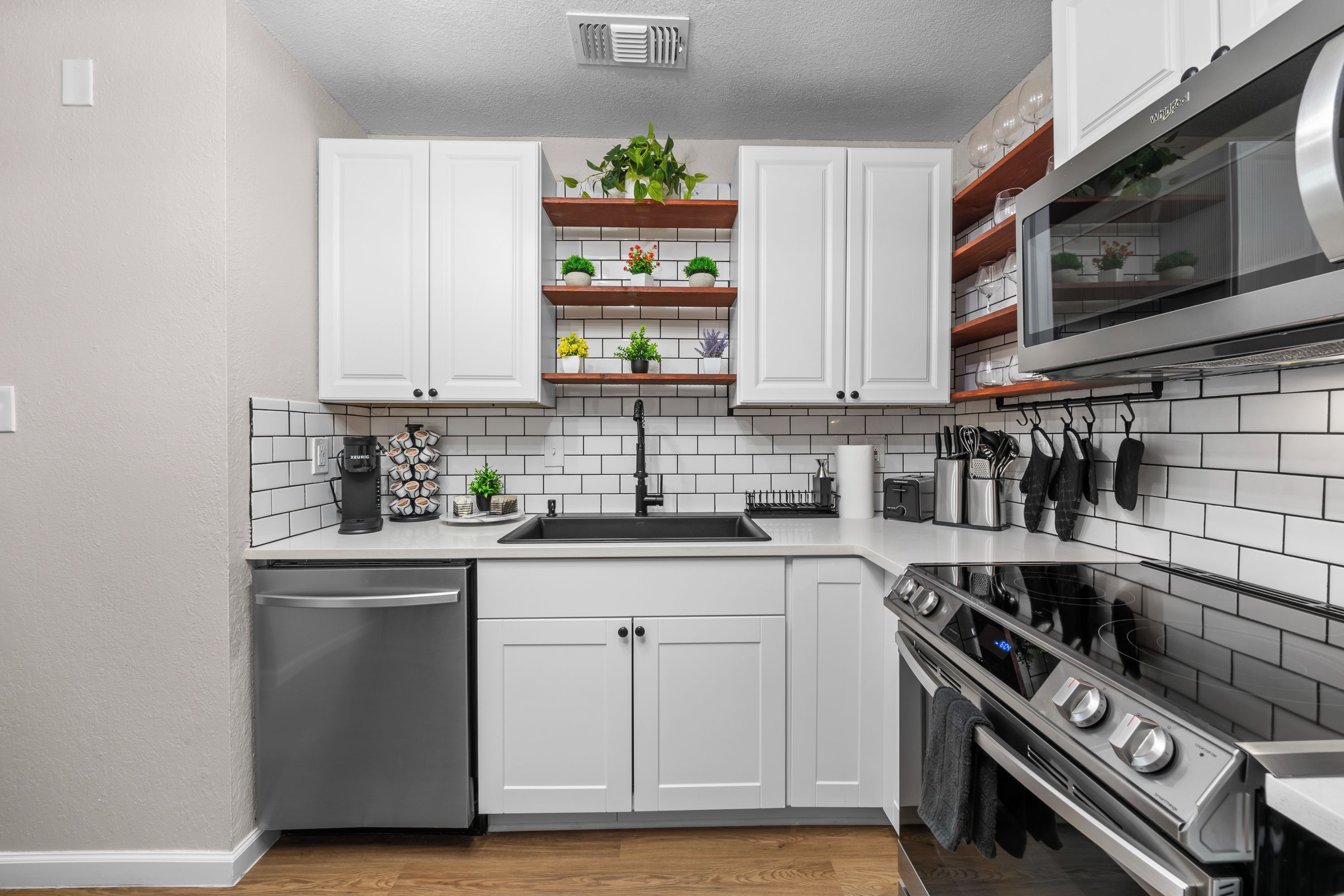 A modern kitchen with white cabinetry, a stainless steel dishwasher, a built-in oven, and a microwave.