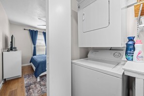 A laundry room with a washing machine, a dryer, and a small cabinet. - AT&T Stadium Area Arlington TX 1 Bed 1 Bath (Arlington)