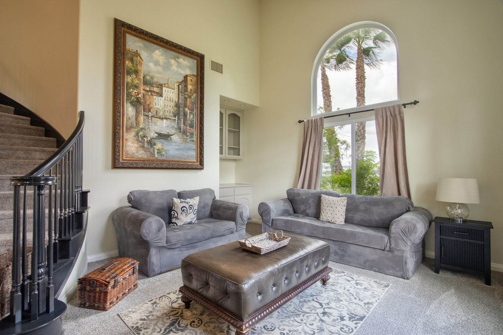 A living room with two grey sofas, a coffee table, wicker baskets, a painting, and a staircase.