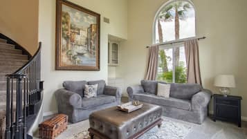 A living room with two grey sofas, a coffee table, wicker baskets, a painting, and a staircase.