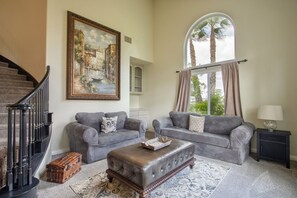 A living room with two grey sofas, a coffee table, wicker baskets, a painting, and a staircase. - Casa de Saudade by Fieldtrip | Wine Country Views, Pool, Waterslide & Hot Tub | Sleeps 10 (Temecula)