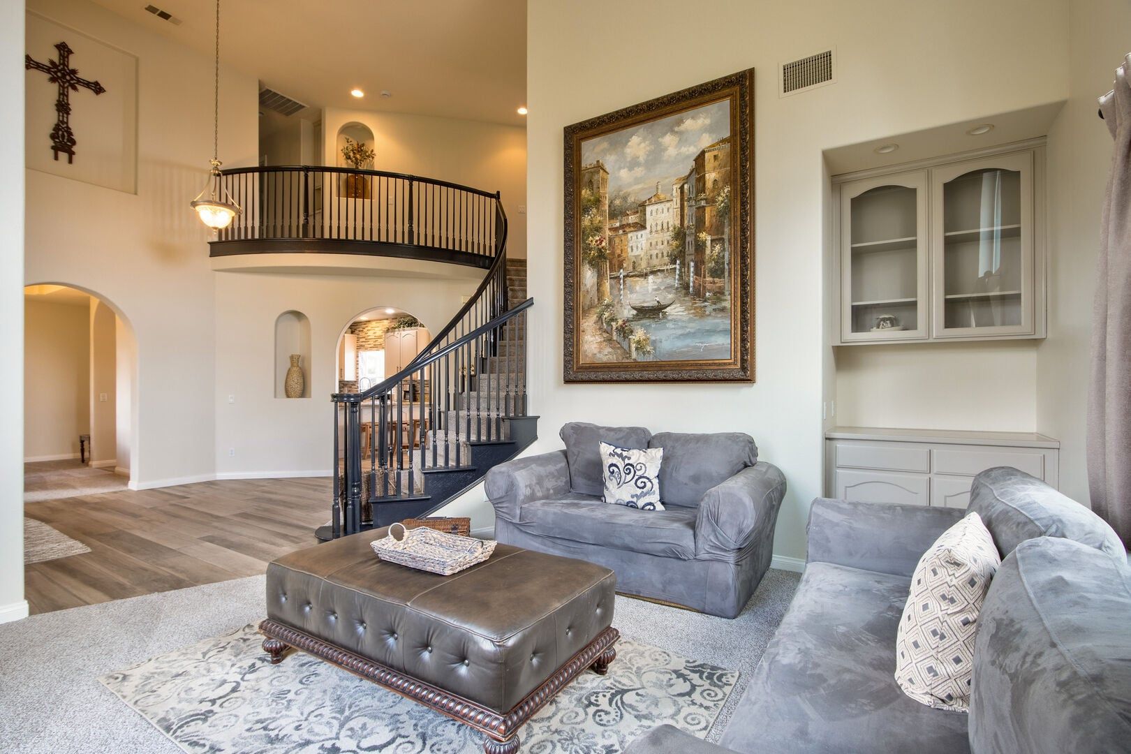 A spacious living room with a grand staircase, a large painting, and a cozy seating area.
