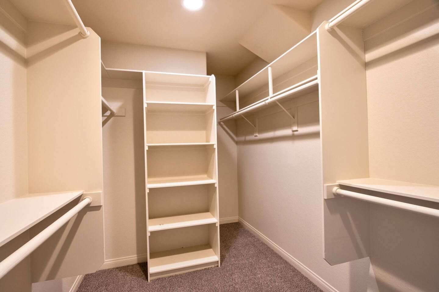 A walk-in closet with multiple shelves and hanging space, carpeted floor, and white walls.