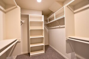 Un dressing accessible sans porte, doté de nombreuses étagères et d’un espace pour suspendre les vêtements, avec un sol recouvert de moquette et des murs blancs.