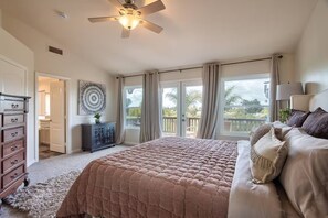 Un dormitorio con una cama grande, ventilador de techo, cómoda y vista al exterior.