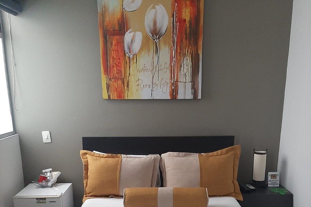 A hotel room with a bed, a nightstand, a lamp, and a painting on the wall.