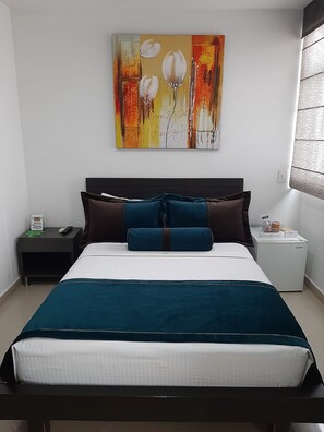 A hotel room with a bed, a nightstand, a bedside table, and a wall-mounted painting. - HOTEL MEDELLIN GOLD (Medellín)