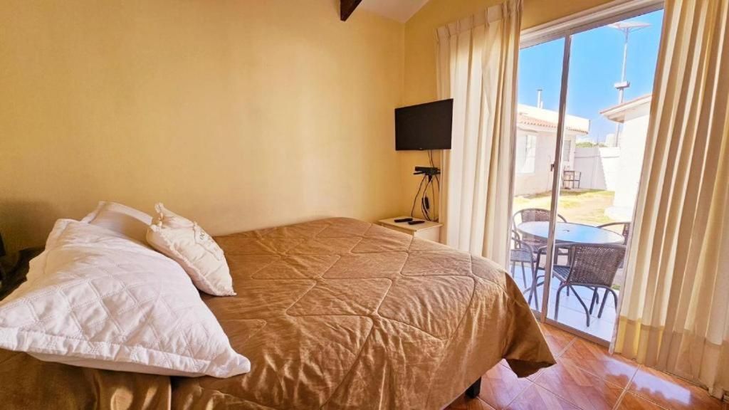 A bedroom with a bed, a TV on a stand, and a view of the outside.