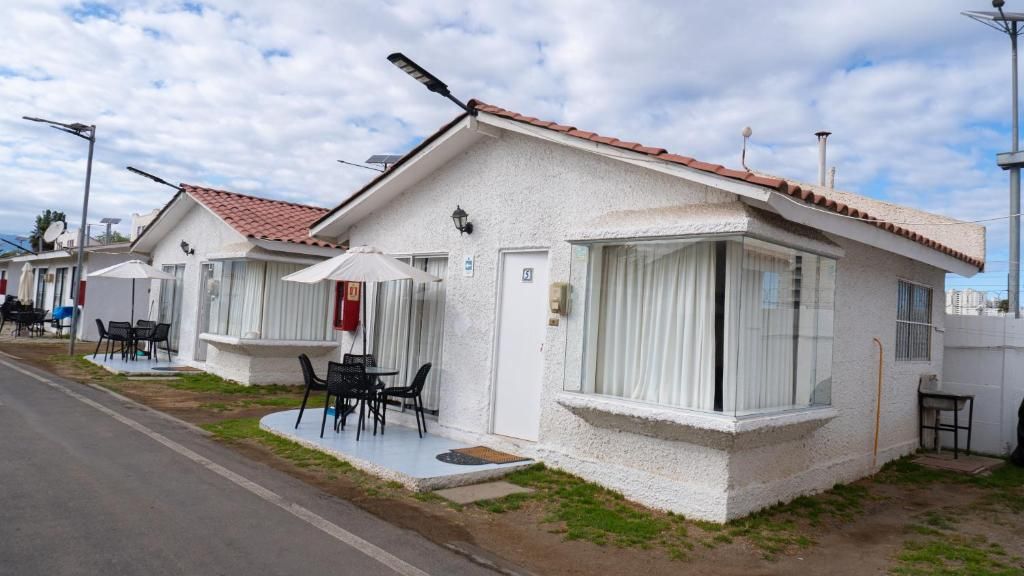 A row of white single-story houses with tiled roofs, each featuring a small patio with a table and chairs.
