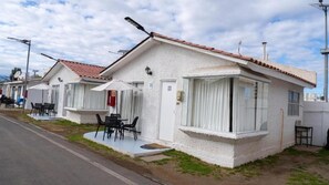 A row of white single-story buildings with tiled roofs, each with a small patio area and outdoor seating. - Cabañas Pinamar  (Elqui)