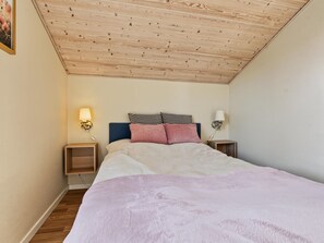 A bedroom with a wooden ceiling, a bed with a pink blanket, two bedside tables with lamps, and a patterned pillow. - "Nelia" - 1km from the sea by Interhome (Væggerløse)