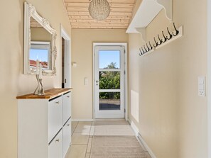 Ein Flur mit einer weißen Tür, einem Spiegel, einem kleinen Tisch mit einer Lampe und einem an der Wand befestigten Kleiderhaken.