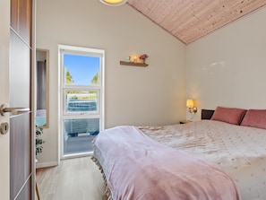 Ein Schlafzimmer mit einem Bett, einem Fenster, einer Tür und einem an der Wand befestigten Regal mit Kerze und Blumen.