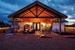 Un espacio al aire libre techado con mesa y sillas, un brasero y una zona de estar con cojines.