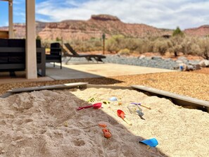 A sandy area with beach toys and a poolside setting with a view of red rock formations. - Family Reunion Ranch Near Zion: 4 Homes, Sleeps 26 (Kanab)