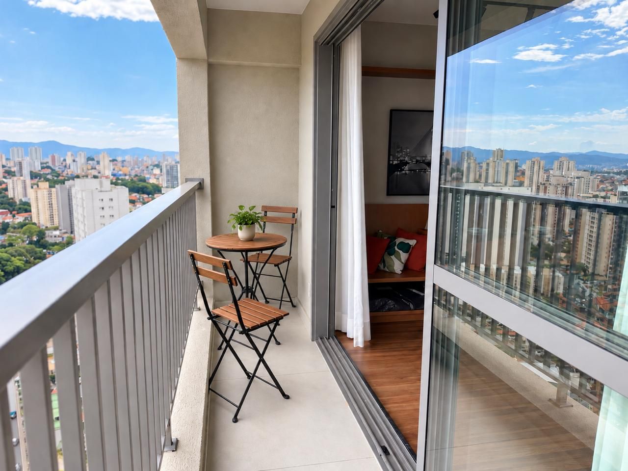 A balcony with a table and chairs, a potted plant, and a city view.