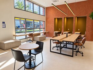A modern conference room with a long table, multiple chairs, and a large window offering a view of the street. - GRU Residence | Cozy studio on the 27th floor, close to the airport. (Guarulhos)