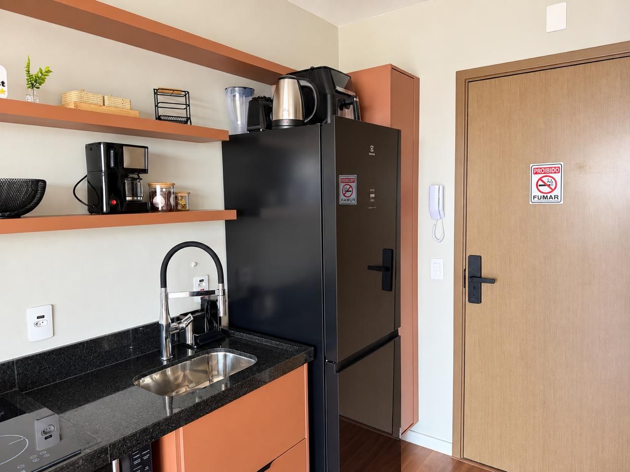 A compact kitchen with a black refrigerator, a coffee maker, and a sink.