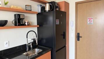 A compact kitchen with a black refrigerator, a coffee maker, and a sink.