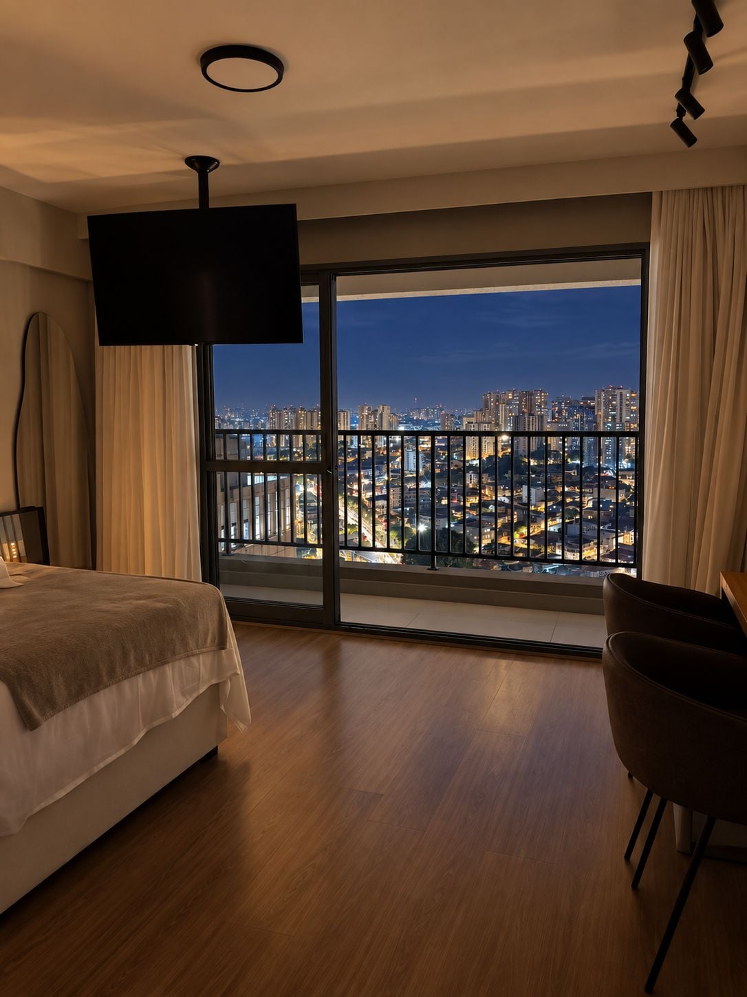 Habitación de hotel con una cama grande, televisión, escritorio y vista a un paisaje urbano desde un balcón.