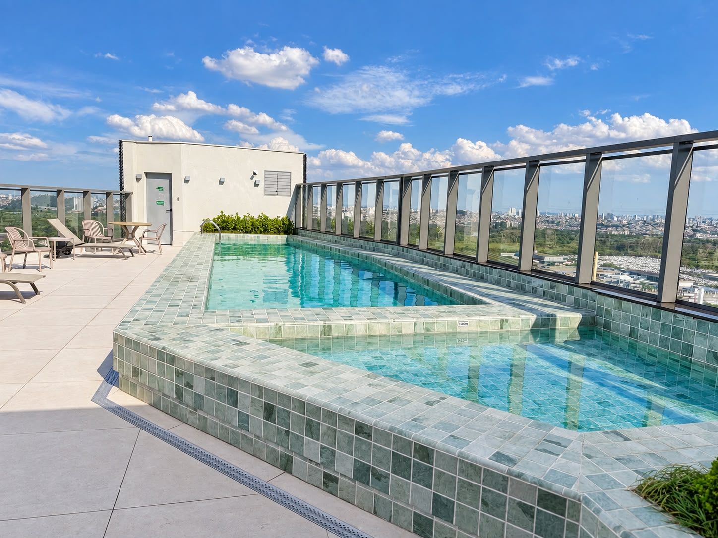 A rooftop pool with clear blue water, surrounded by glass railings and a city view.