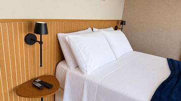 Quarto de hotel com cama, mesa de cabeceira com controle remoto e luminária na parede.