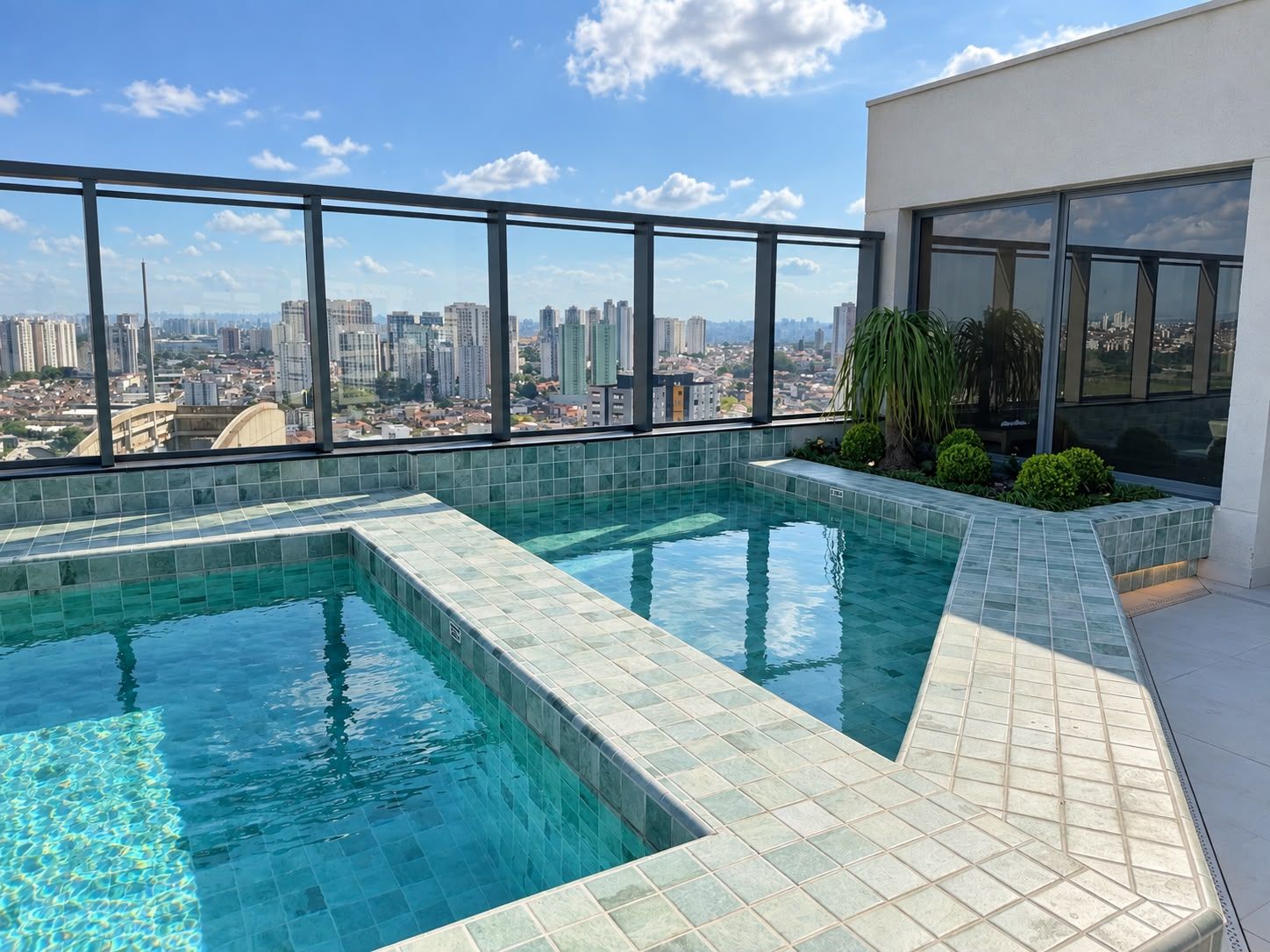 Piscina no terraço com vista para a cidade, rodeada por guarda-vidro e fachada de um edifício moderno.
