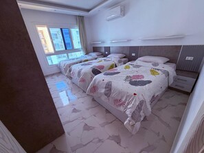 A hotel room with two beds, a window with curtains, a flat-screen TV, and a modern air conditioning unit. - Fanadir Bay Luxury Sea View Apartment (Hurghada)