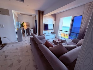 A modern living room with a sofa, a flat-screen TV, and a view of the ocean. - Fanadir Bay Luxury Sea View Apartment (Hurghada)