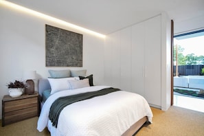 A modern bedroom with a large bed, a nightstand, a wall-mounted artwork, and a sliding glass door leading to an outdoor area. - Asgard Luxury Escape (Kings Meadows)