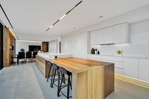 A modern kitchen with a wooden island, bar stools, and white cabinetry. - Asgard Luxury Escape (Kings Meadows)