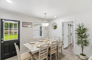 A dining area with a white table set for four, a chandelier, and a potted plant. - Relaxing 4-Bedroom Fort Walton Beach Retreat Stylish Baths & Family Comfort (Fort Walton Beach)