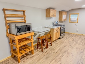A compact kitchen with wooden cabinetry, a built-in microwave, a stove, and a small wooden table with stools. - Taurus | Black Lake Glamping Dome (Hammond)