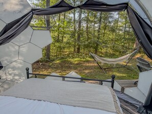 A tent with a bed inside, a hammock outside, and a forest view. - Taurus | Black Lake Glamping Dome (Hammond)