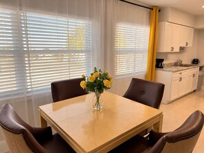 Een eetgedeelte met een tafel, stoelen en een vaas met gele bloemen.