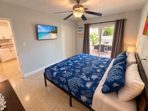 Un dormitorio con cama, ventilador de techo, televisor en la pared y vista al exterior.