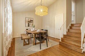 A dining area with a wooden table, chairs, a bench, a hanging light fixture, a framed picture on the wall, and a staircase. - Peaceful 4BR Home Private Backyard Near DC & Old Town (Alexandria)