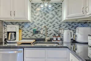 Een moderne keuken met witte kastjes, een betegelde spatwand en diverse apparaten, waaronder een koffiezetapparaat en een broodrooster.