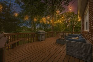 A wooden deck with a grill and outdoor seating, surrounded by trees and string lights. - Peaceful 4BR Home Private Backyard Near DC & Old Town (Alexandria)