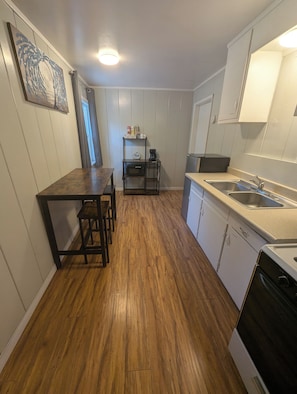 Una cocina compacta con piso de madera, una mesa de comedor con sillas, una cafetera y un lavamanos.