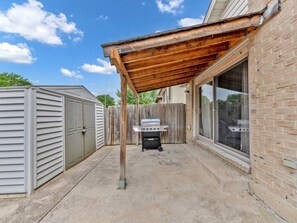 A covered patio area with a grill, a storage shed, and a brick wall. - 4BR Home | Fenced Yard & 2-Car Parking (Windsor)