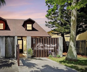 A two-story building with a wooden fence, a sign reading 'The Surf House,' and a number '210' on the fence. - 2 Bed two bath loft, king beds, full chef kitchen & Backyard (Cape Canaveral)