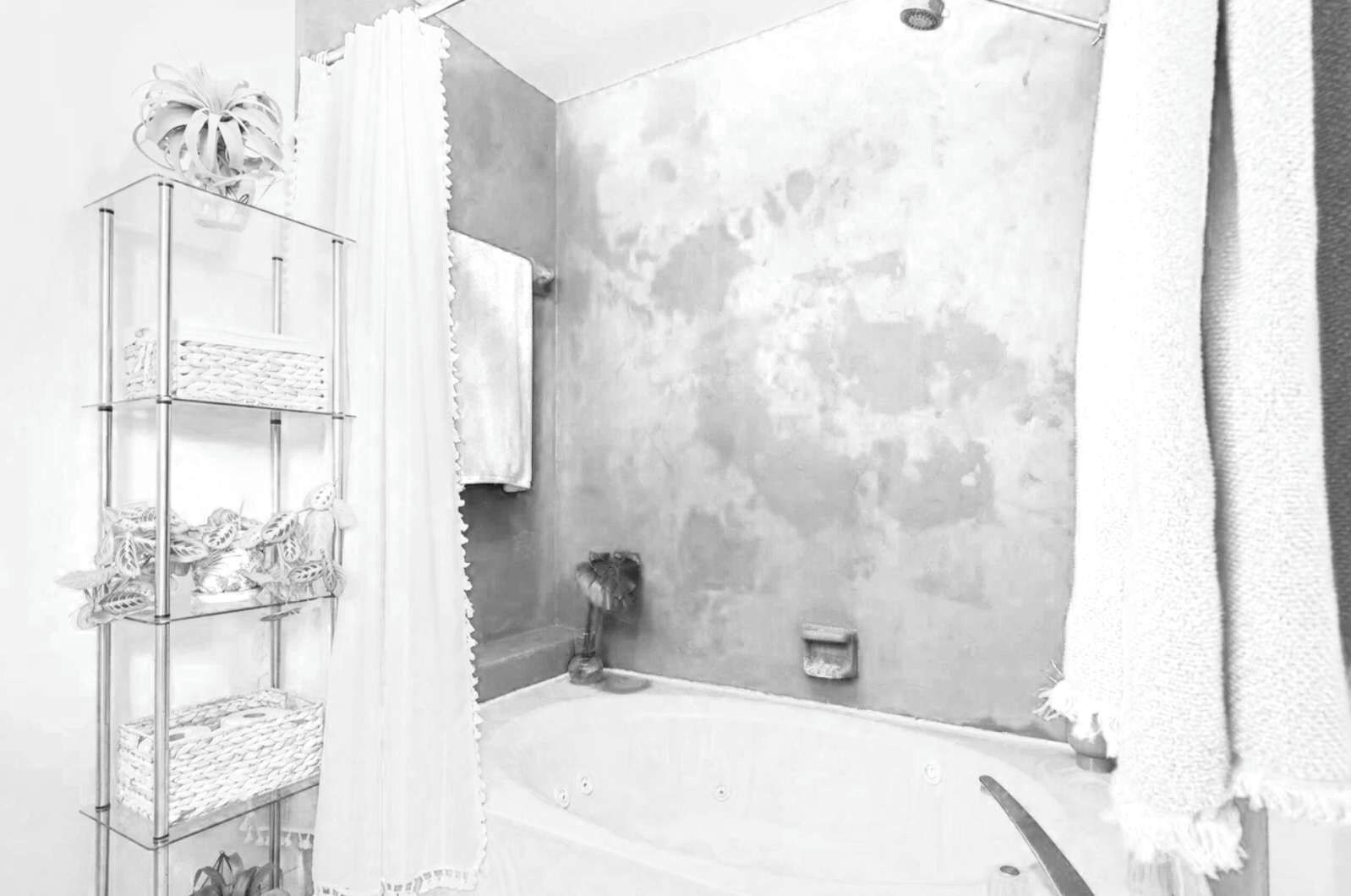 A bathroom with a bathtub, a glass shelf with towels, and a shower area.