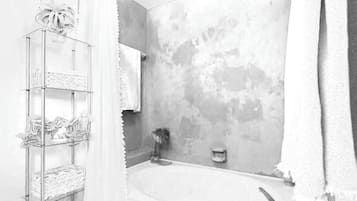 A bathroom with a bathtub, a glass shelf with towels, and a shower area.