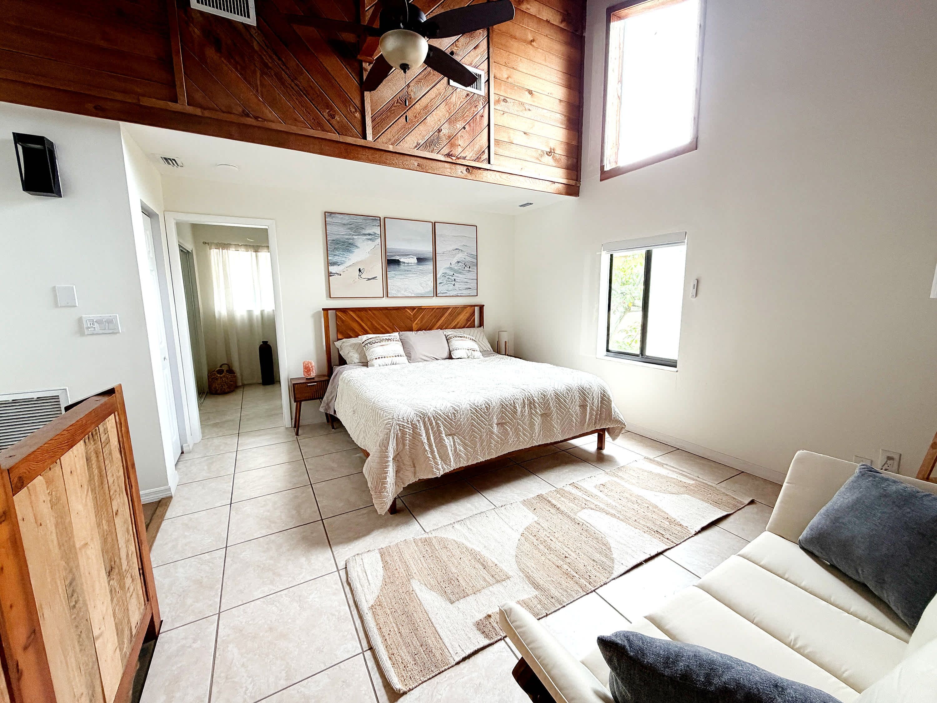 A bedroom with a bed, a sofa, a ceiling fan, and a window.