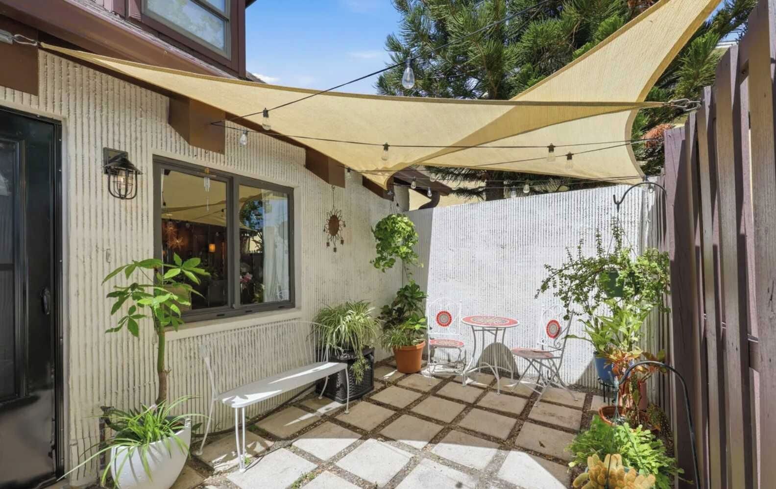 A patio with a table and chairs, potted plants, and a pergola providing shade.