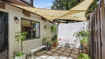A patio with a table and chairs, potted plants, and a pergola providing shade.