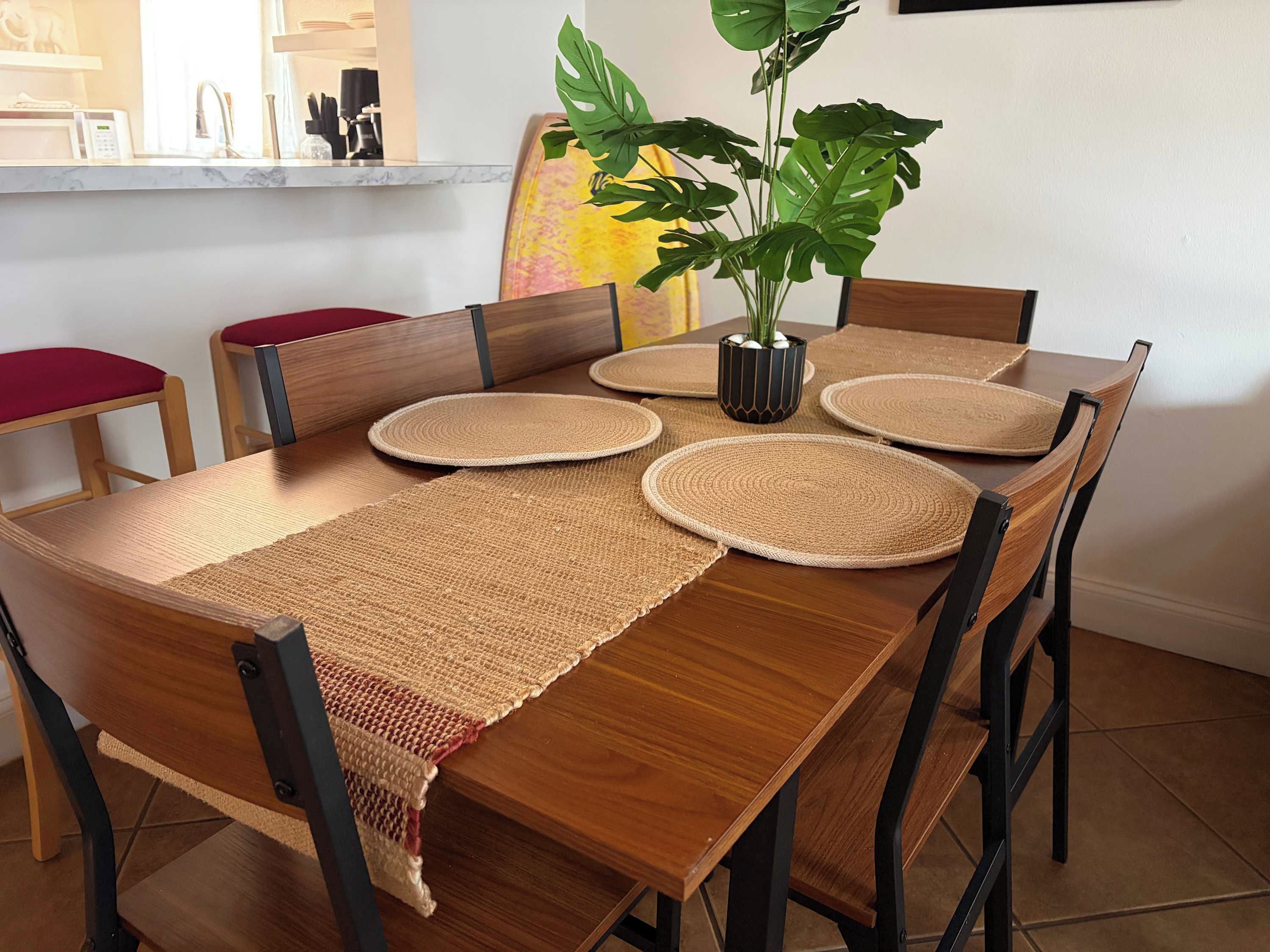 A dining table with a woven placemat, surrounded by chairs with black frames and red cushions.